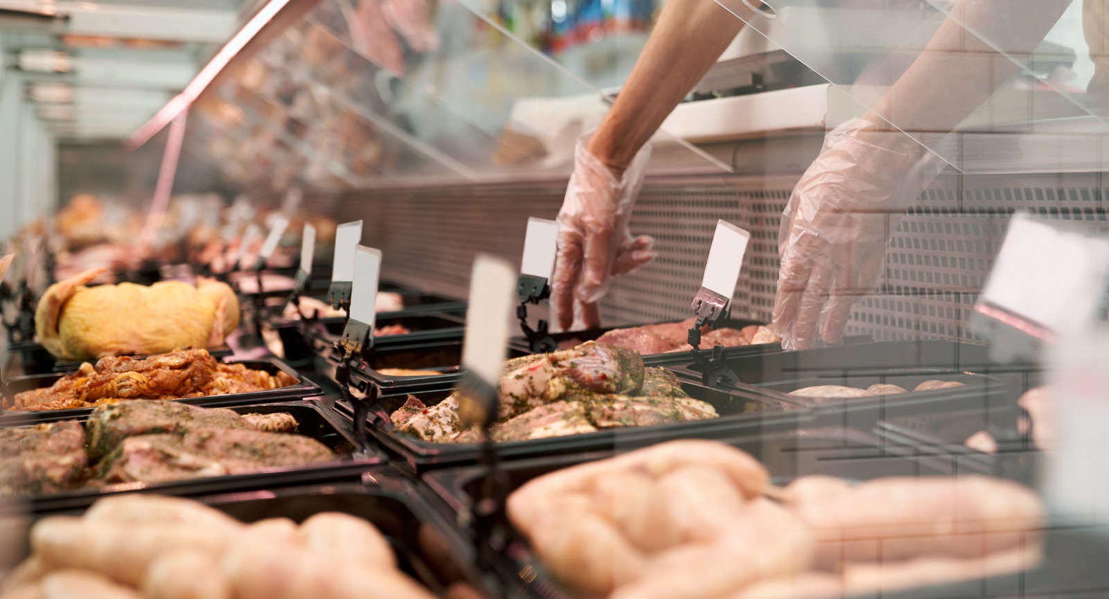 fresh meat in a deli display with gloved hands reaching in to stock