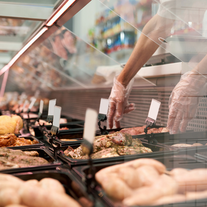 fresh meat in a deli display with gloved hands reaching in to stock